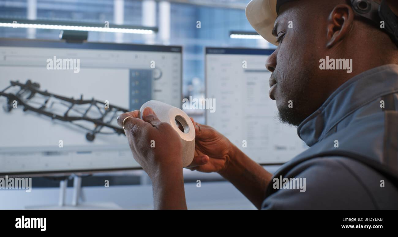 Ingeniero verifica le dimensioni di un componente lavorato rispetto al modello CAD su monitor, combinando la misurazione fisica con la tecnologia del gemello digitale per la produzione robotizzata, il prototipaggio, la metrologia e il design. Foto Stock