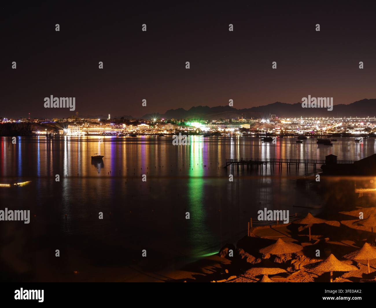 Vista notturna di Sharm el Sheikh, Egitto, con luci che si riflettono sul Mar Rosso e montagne che si stagliano contro il cielo serale Foto Stock