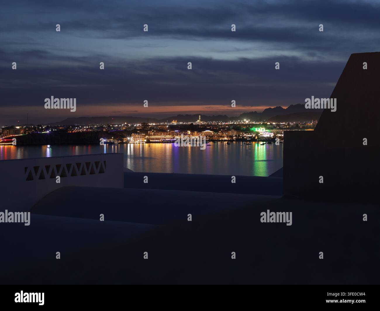 Vista notturna di Sharm el Sheikh, Egitto, con luci che si riflettono sul Mar Rosso e montagne che si stagliano contro il cielo serale Foto Stock