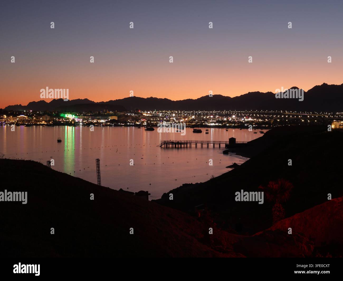 Vista notturna di Sharm el Sheikh, Egitto, con luci che si riflettono sul Mar Rosso e montagne che si stagliano contro il cielo serale Foto Stock