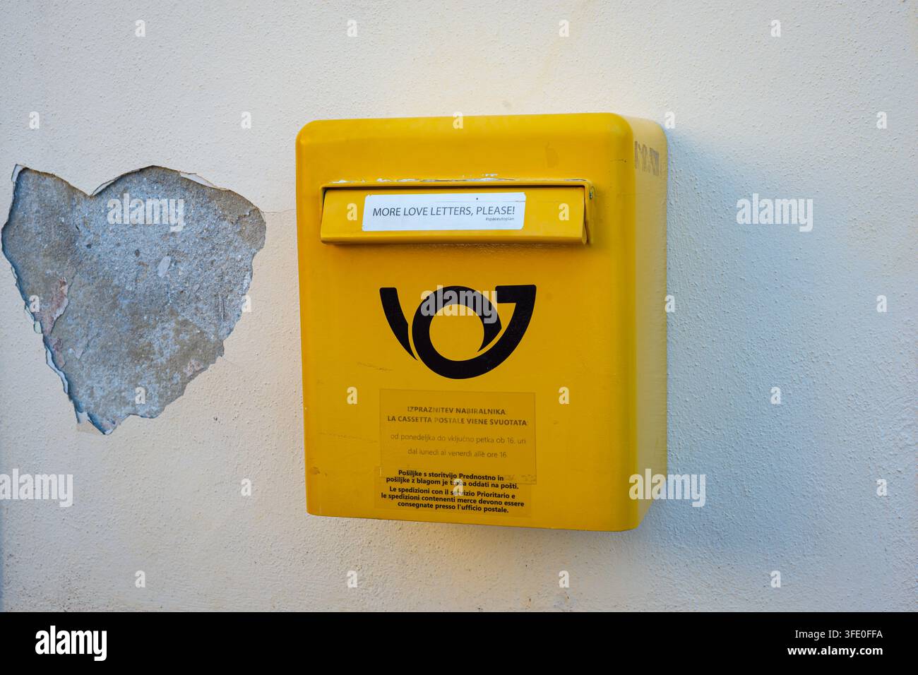 Cassetta delle poste gialla su muro intonacato con vernice sbucciata a forma di cuore e fessura per lettere d'amore. Foto Stock