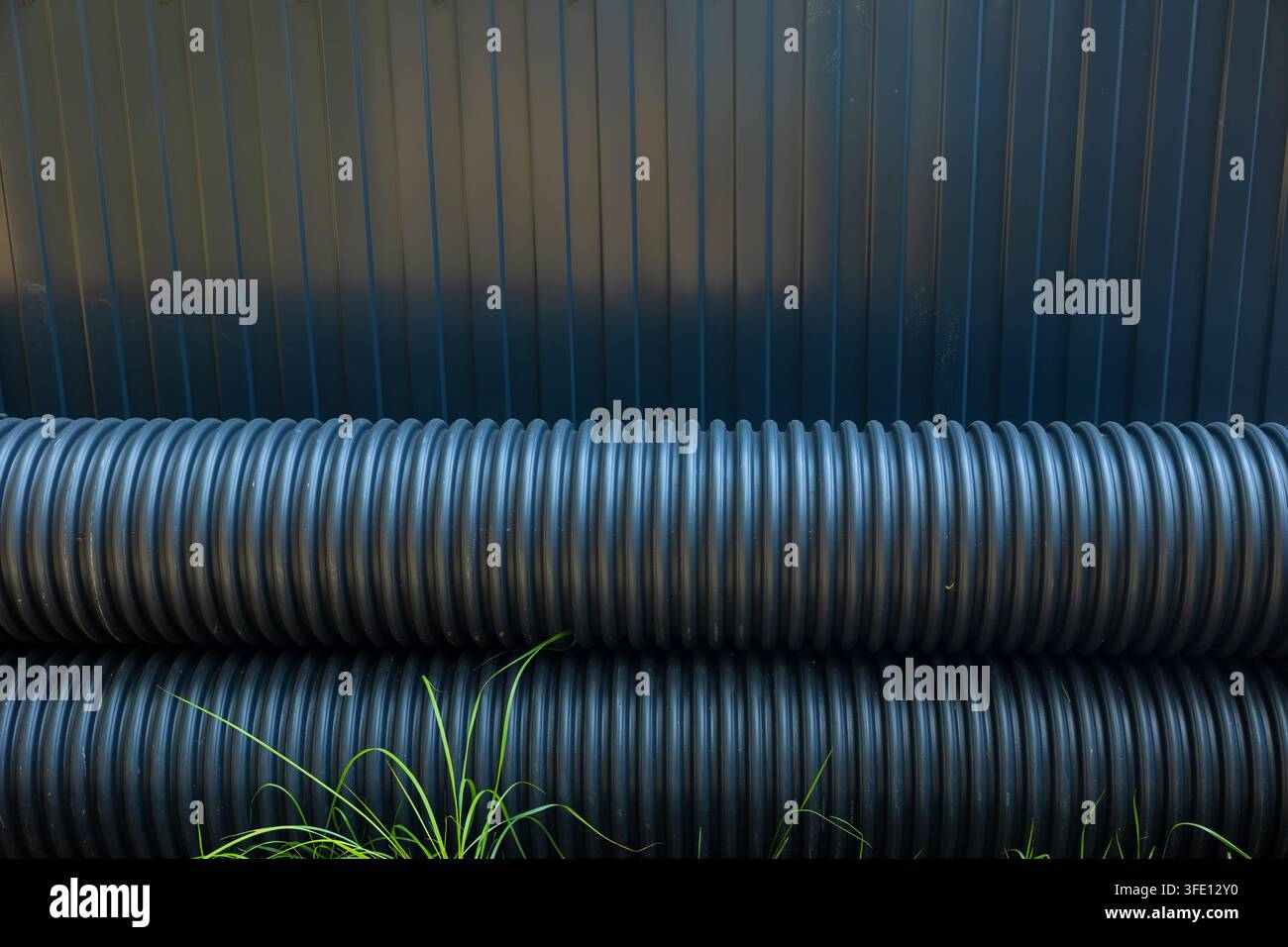 Tubi di plastica ondulata neri impilati riposti accanto al muro all'aperto, infrastrutture di drenaggio e materiali da costruzione. Foto Stock