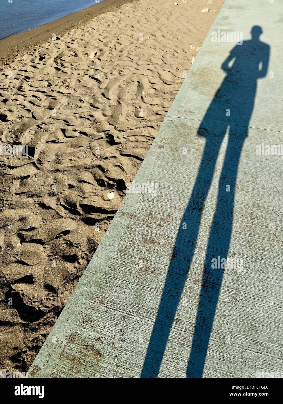 Ombra di una figura su un sentiero di cemento accanto alla spiaggia sabbiosa e al mare, Costa Dalmata, Croazia - Immagine stock catturata con smartphone