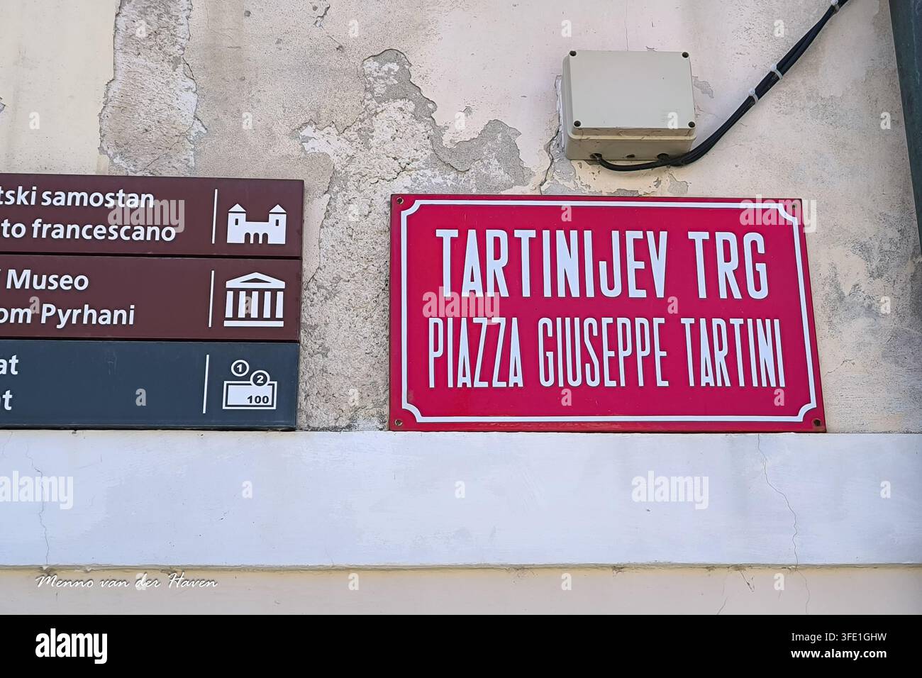 Segnale stradale con l'iscrizione Tartinijev Trg, Piazza Giuseppe Tartini montato su un muro di intonaco invecchiato con pannelli direzionali per turisti nella storica Piran, in Slovenia. Foto Stock