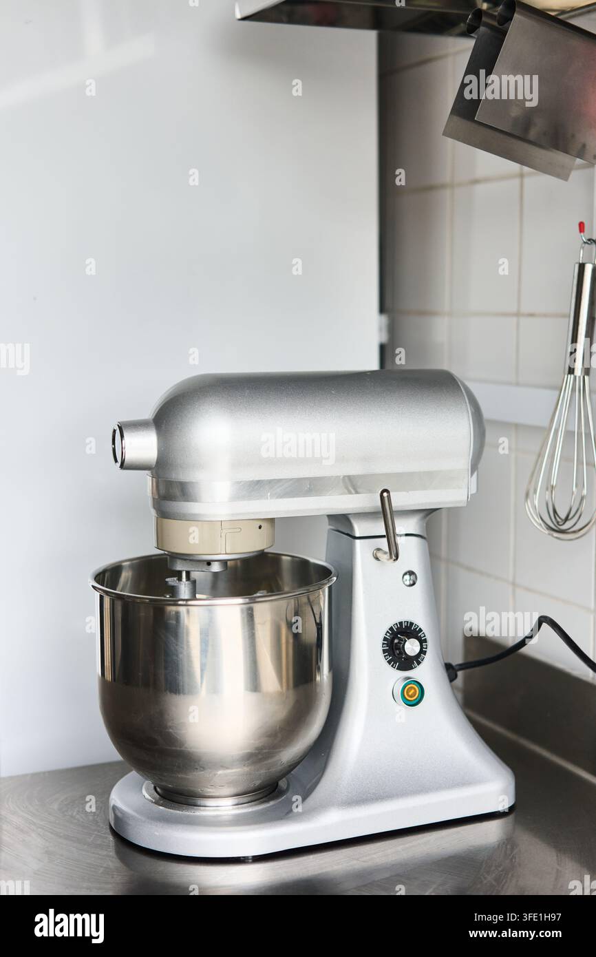Miscelatore da banco commerciale su bancone in acciaio inossidabile in cucina piastrellata con frusta appesa, con miscelatore, supporto, commerciale, dettaglio della cucina, mostra la ciotola del miscelatore Foto Stock