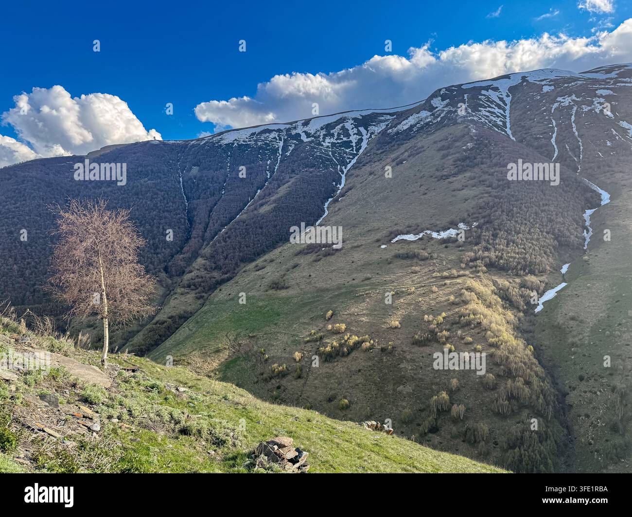 Paesaggio montano primaverile vicino a Stepantsminda a Kazbegi, in Georgia, con neve che si scioglie sui pendii del Caucaso sotto un cielo blu vivido. - Immagine stock catturata con smartphone