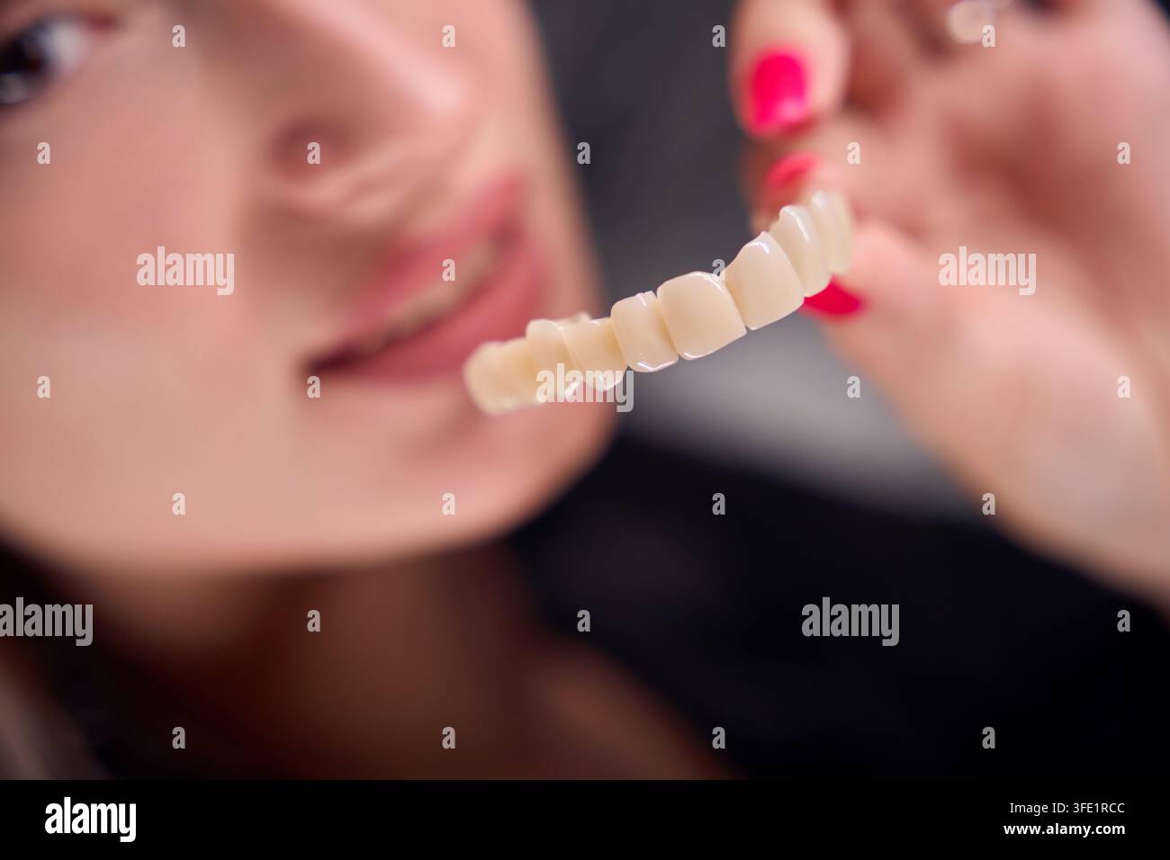 Donna adulta concentrata tiene una protesi dentale in uno studio dentistico professionale. Un sorriso sottile riflette sicurezza e attenzione alla salute dentale cosmetica. Foto Stock