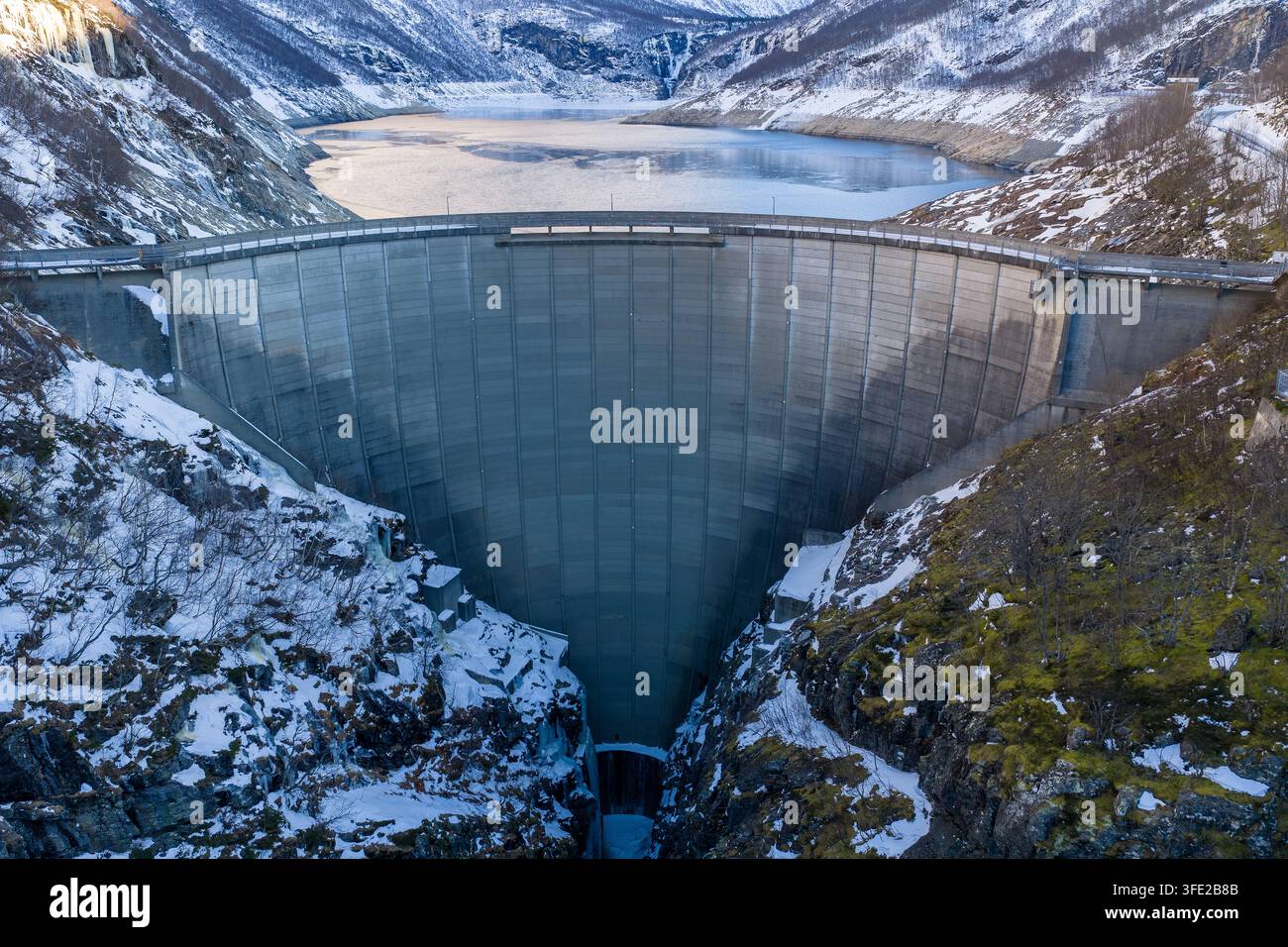 Vista aerea della diga di cemento incastonata tra pendici montuose coperte di neve e scogliere ghiacciate a Tafjord, More og Romsdal, Norvegia. Foto Stock