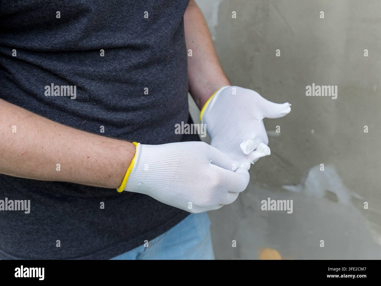 Una persona indossa guanti da lavoro bianchi con bordi gialli. Le mani mostrano una preparazione attenta e concentrata Foto Stock