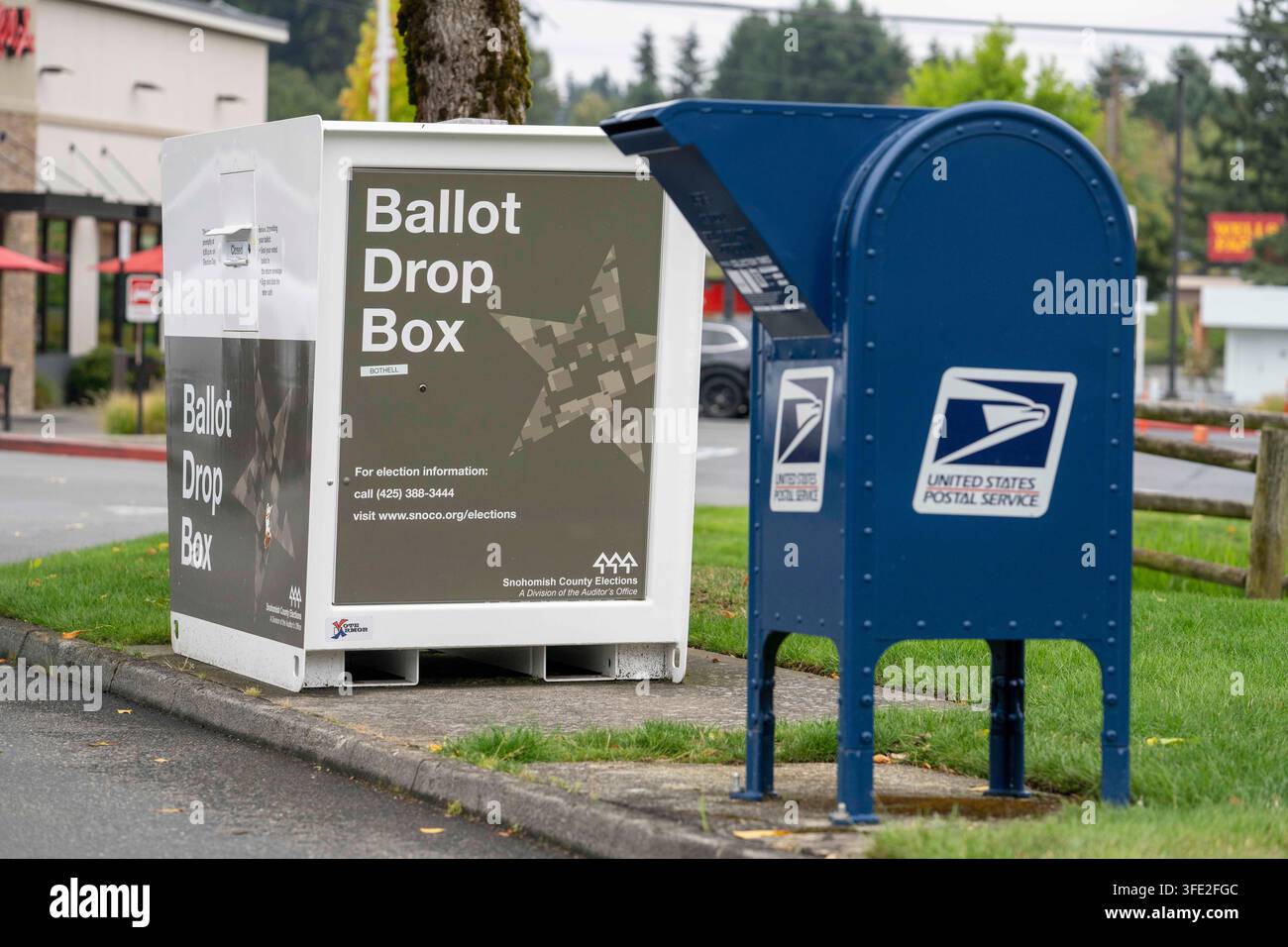 Bothell, Washington, USA. 1 set., 2026. Una cassetta di raccolta USPS blu si trova accanto a una cabina per il deposito delle schede elettorali della contea di Snohomish al margine di un parcheggio a Bothell, Washington, USA, martedì 1 settembre 2026. Oltre il 98% degli elettori dello stato di Washington utilizza il sistema di voto per posta, anche se una grande percentuale di elettori utilizza cabine per il deposito delle schede elettorali come questa invece di inviarle tramite il servizio postale. La fessura per l'inserimento ha un cartello "chiuso" perché non è in corso un'elezione attiva. L'amministrazione Trump ha cercato di limitare il voto per posta attraverso ordini esecutivi e nuove regole su come le Foto Stock