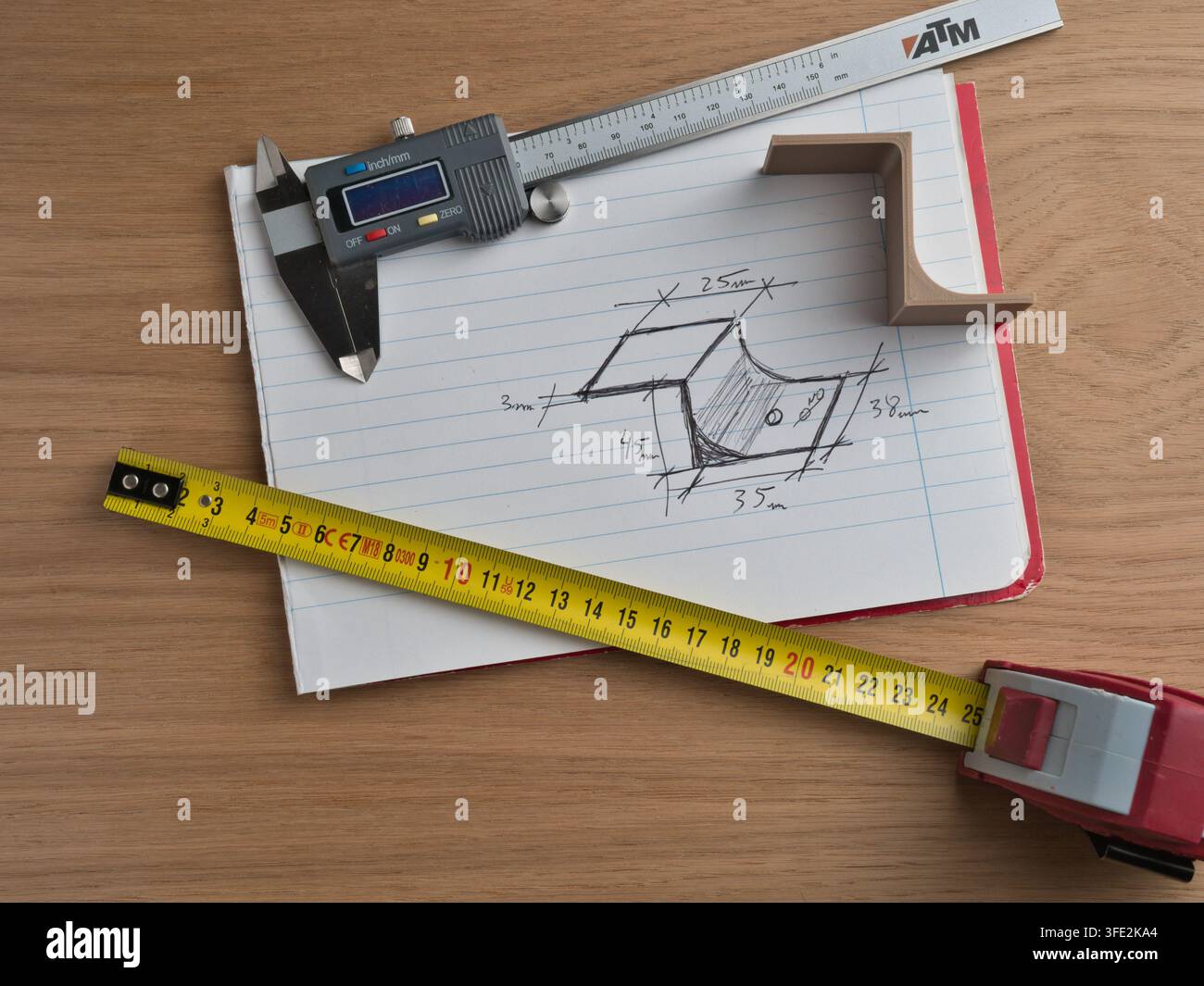 Strumenti di ingegneria e schizzo tecnico – Calibro digitale, metro a nastro e righello circondano uno schizzo tecnico disegnato a mano con dimensioni su uno sfondo di legno Foto Stock