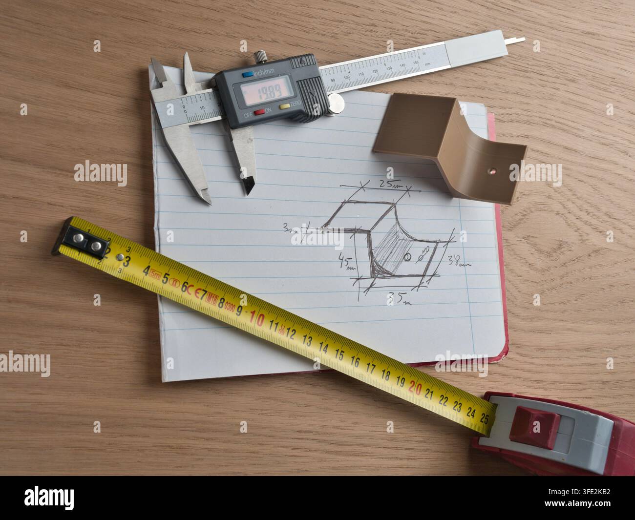 Strumenti di ingegneria e schizzo tecnico – Calibro digitale, metro a nastro e righello circondano uno schizzo tecnico disegnato a mano con dimensioni su uno sfondo di legno Foto Stock