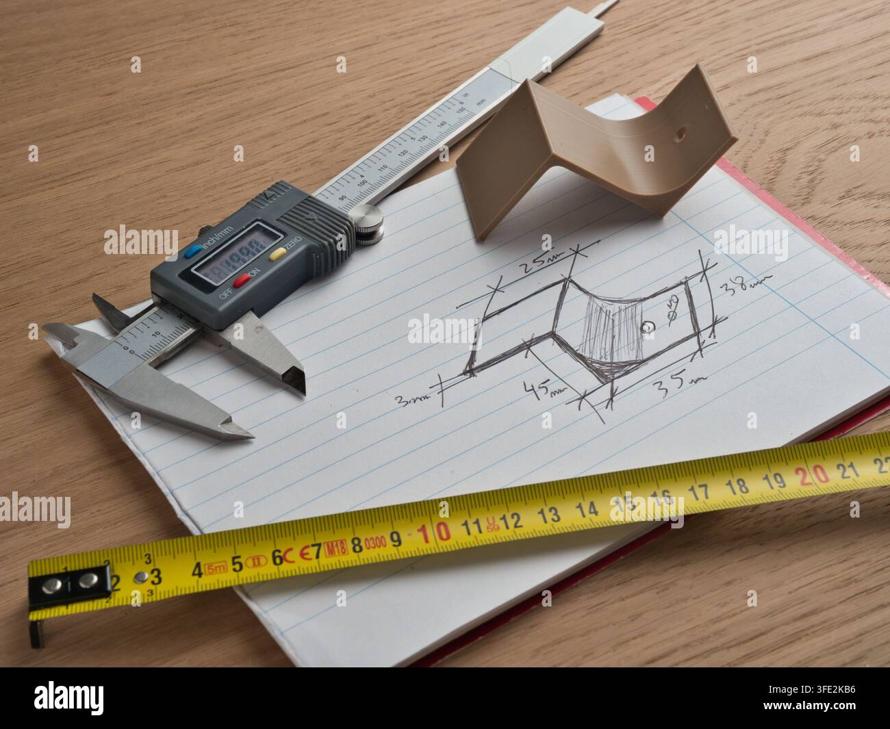 Strumenti di ingegneria e schizzo tecnico – Calibro digitale, metro a nastro e righello circondano uno schizzo tecnico disegnato a mano con dimensioni su uno sfondo di legno Foto Stock