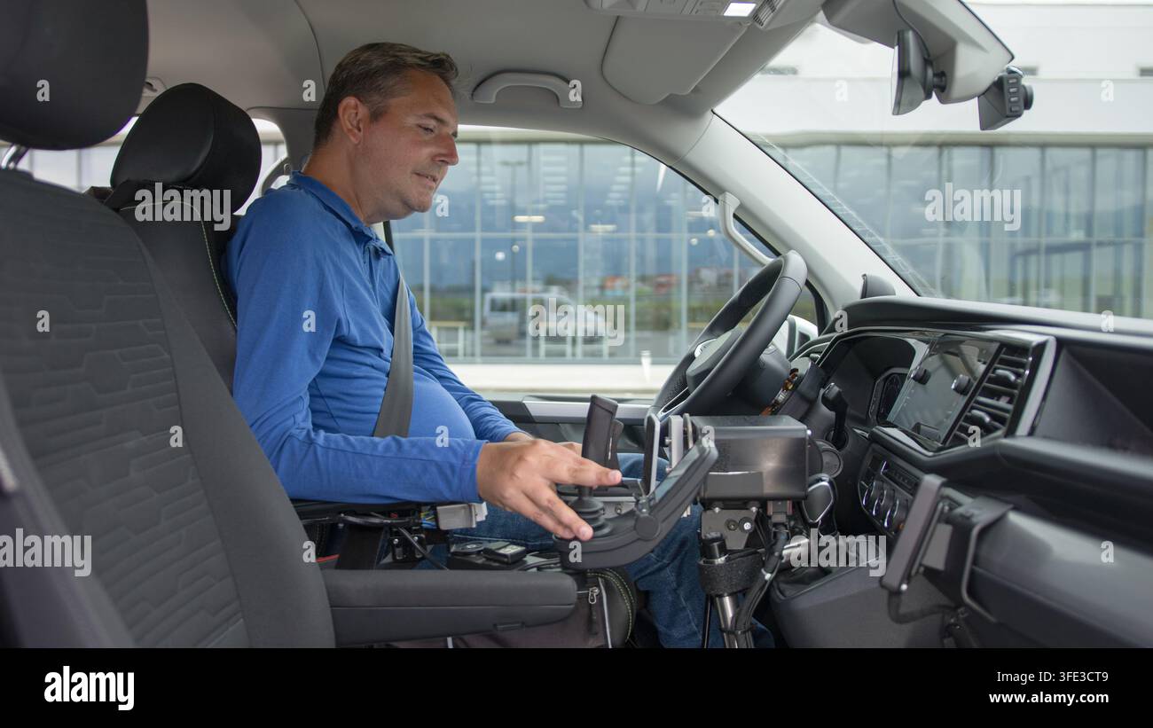 Un uomo con una disabilità utilizza un'auto adattata per guidare in modo indipendente in un luogo urbano. Il veicolo è dotato di tecnologia assistenziale per la mobilità. Foto Stock