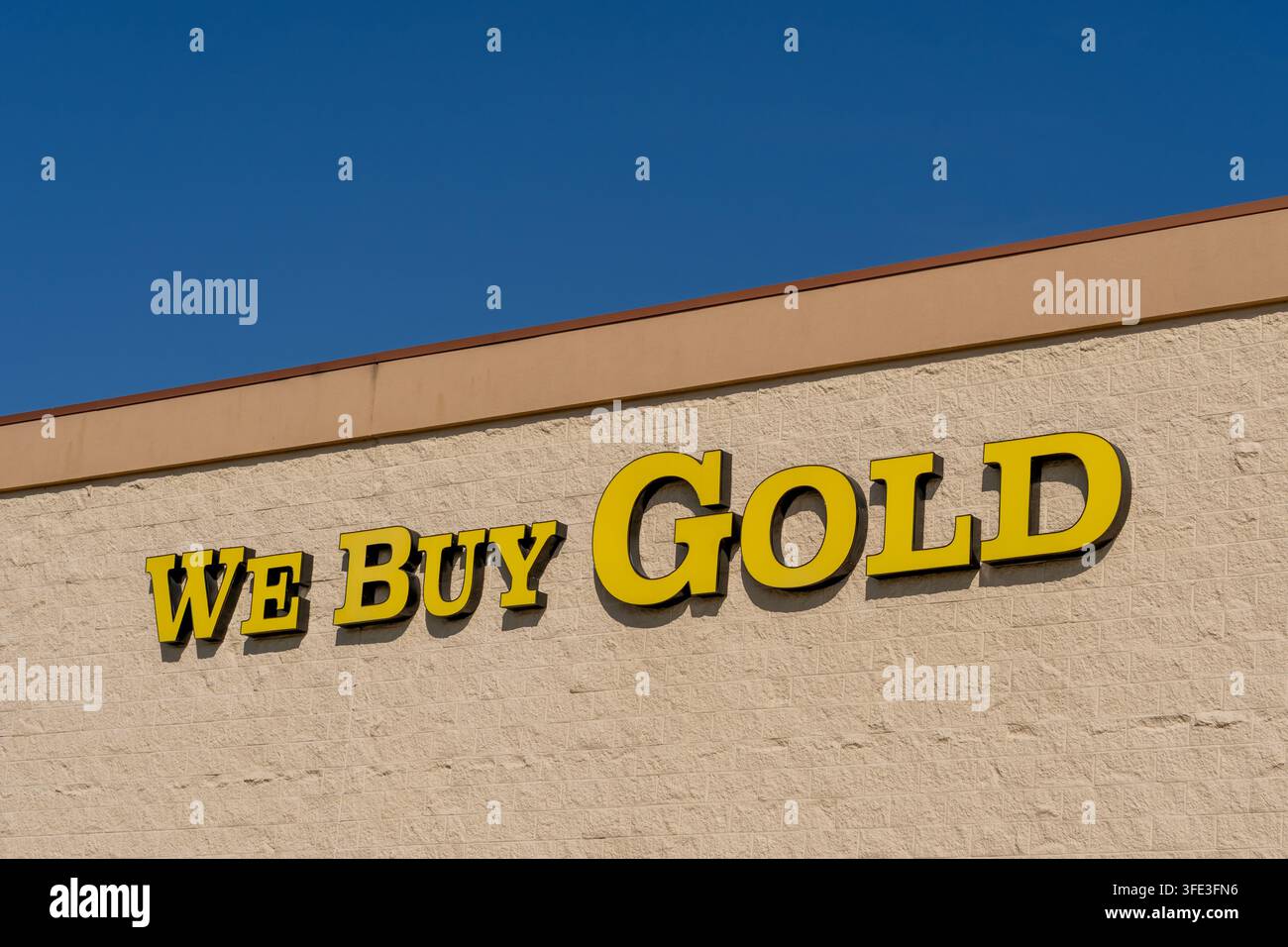 Un'insegna di negozio con la scritta "COMPRAAMO ORO" con lettere gialle montata su un muro beige ruvido sotto un cielo blu. Foto Stock