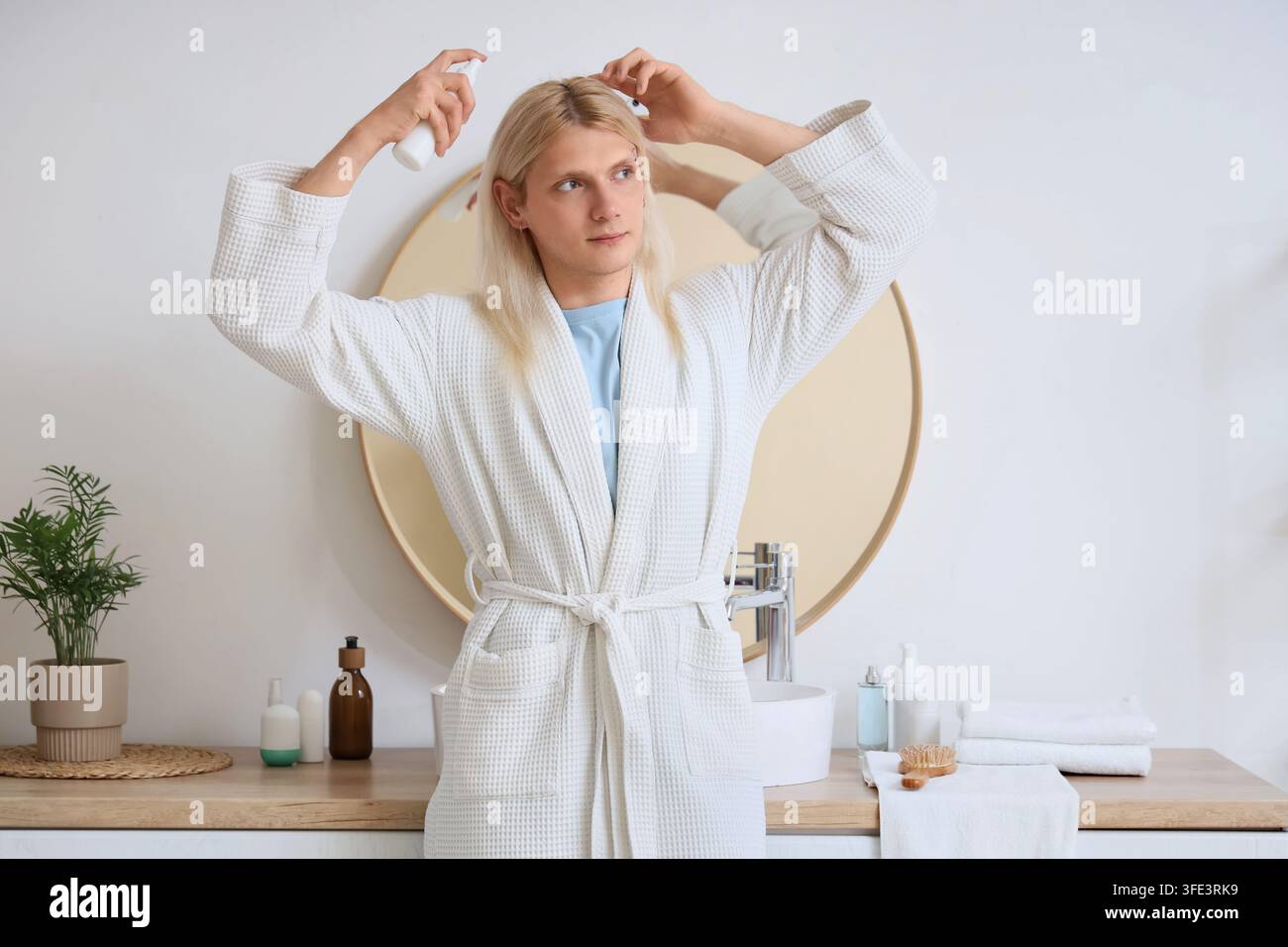 Giovane biondo con spray per capelli in bagno Foto Stock