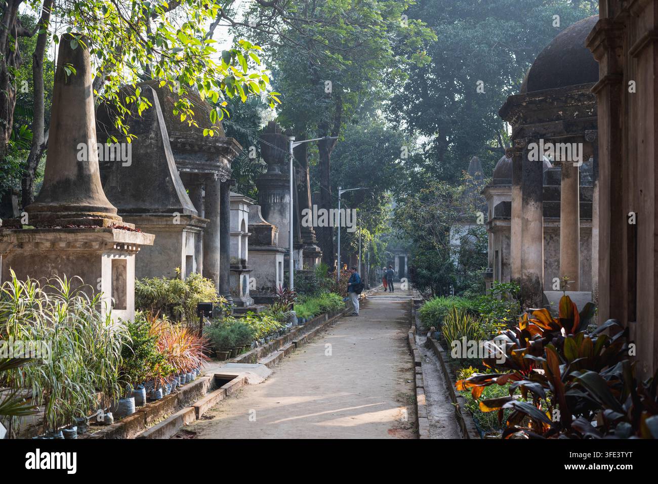 Kolkata, India – 7 gennaio 2026: Lapidi e mausolei dell’era coloniale erosi si ergono tra gli alberi del cimitero di South Park Street Foto Stock