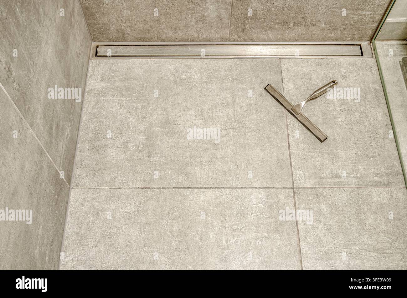 Spazzolino di metallo su piastrelle di pietra grigie in una doccia walk-in moderna Foto Stock