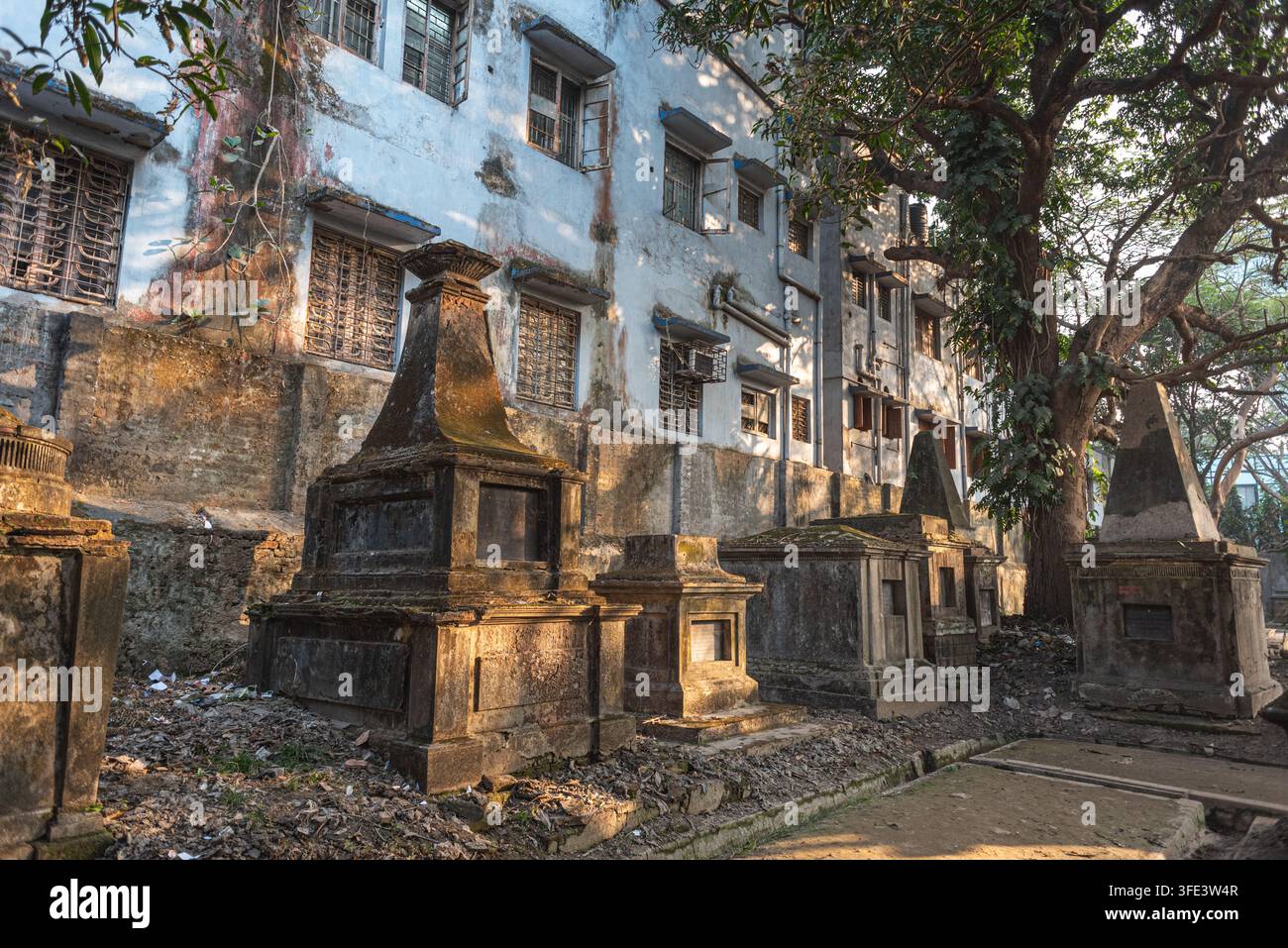 Kolkata, India – 7 gennaio 2026: Lapidi e mausolei dell’era coloniale erosi si ergono tra gli alberi del cimitero di South Park Street Foto Stock