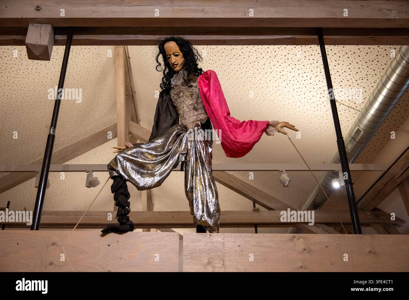 Bad Kreuznach, Germania - 6 set. 25: Marionetta in costume con abiti metallici e manica rossa esposta sopra una ringhiera di legno al PUK Museum für Puppen Foto Stock