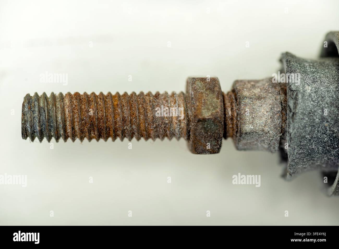 Una fotografia macro dettagliata di un bullone in acciaio fortemente arrugginito con dadi esagonali corrotti, che mostra la texture metallica, il degrado e l'ossidazione su uno sfondo neutro Foto Stock