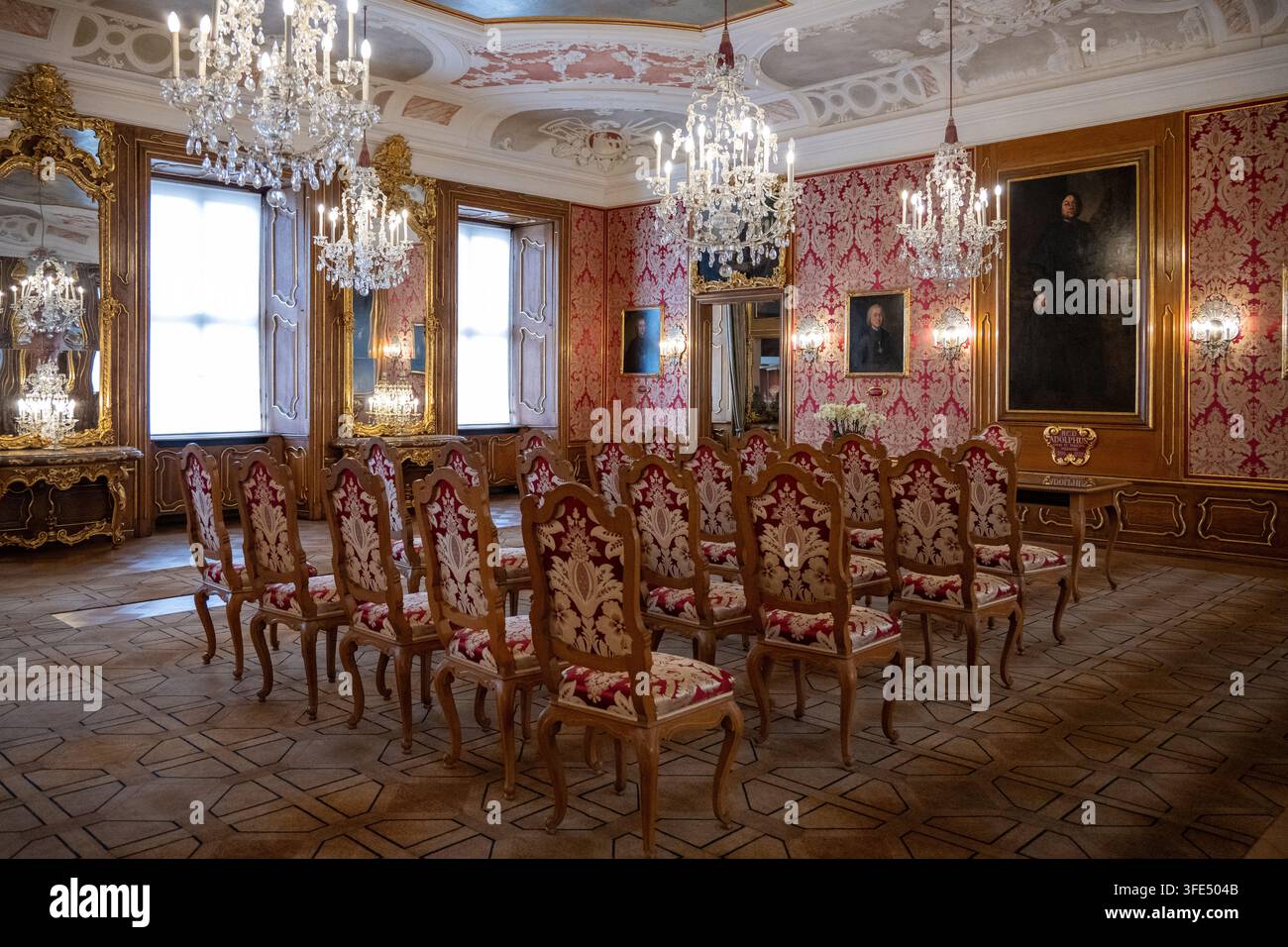 Fulda, Germania - 28 set. 25: Sala cerimoniale storica con lampadari di cristallo, pareti in damasco rosso, ritratti, specchi e file di sedie imbottite a Foto Stock