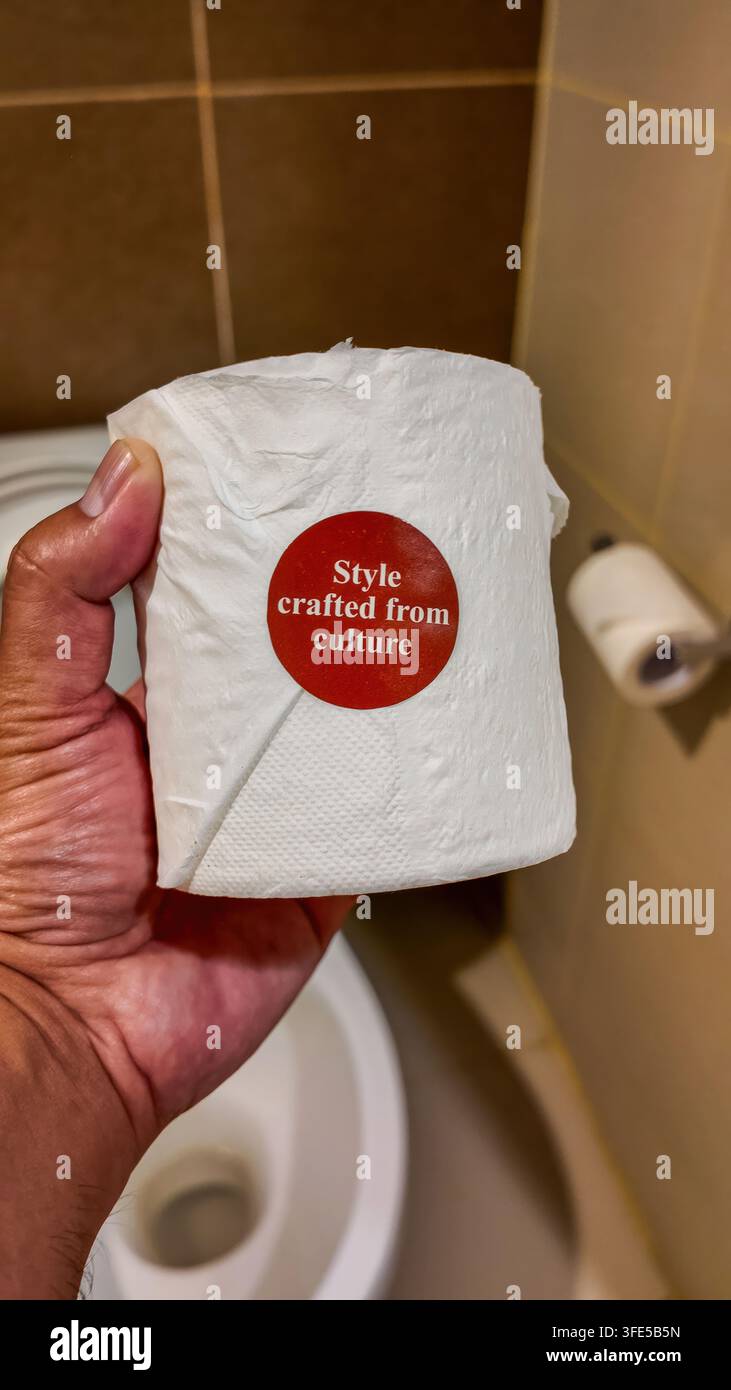 Primo piano di una mano che tiene un rotolo di carta igienica con adesivo promozionale nel bagno di un hotel Foto Stock