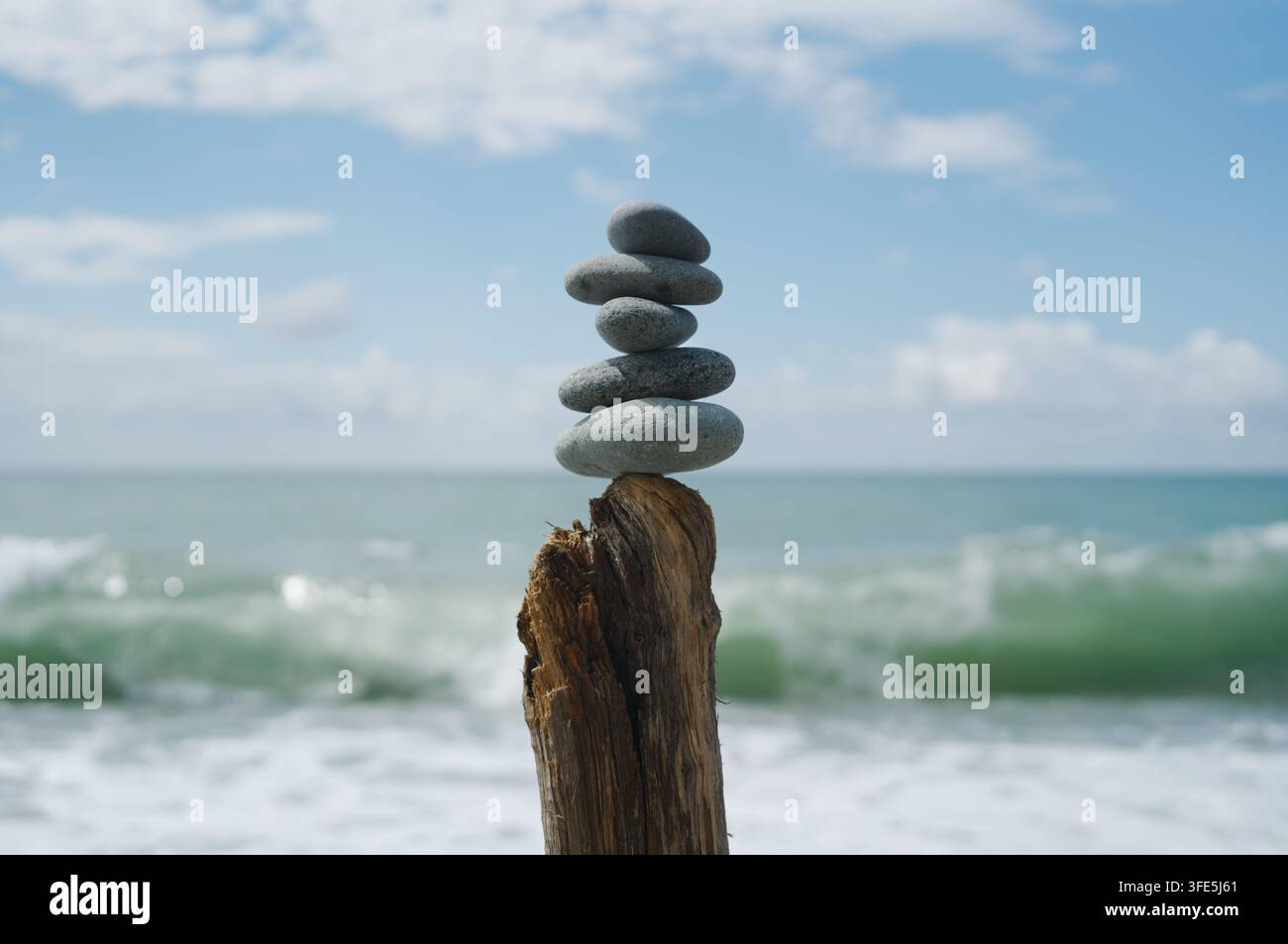 Una pila di pietre bilanciate su un tronco stagionato contro uno sfondo sfocato di mare e cielo. Foto Stock