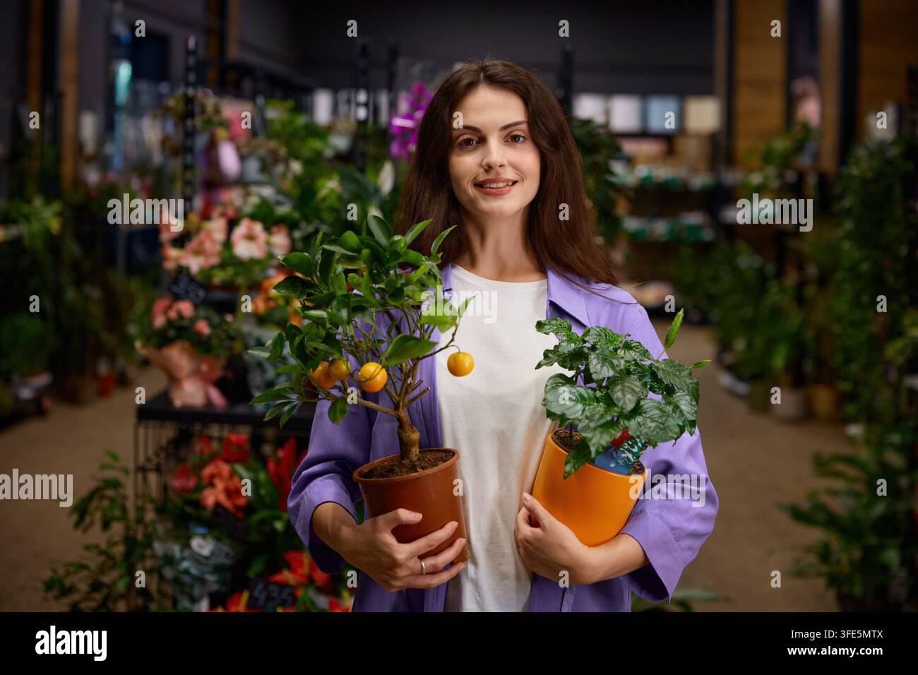 Giovane donna che presenta agrumi in vaso e edera rampicante in un ambiente di negozio Foto Stock