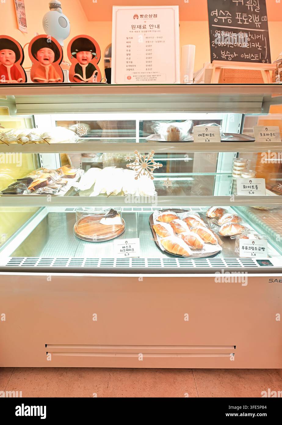 Una vetrina refrigerata per prodotti da forno in Corea che mostra vari pani, torte e pasticcini con cartelli in coreano. Foto Stock