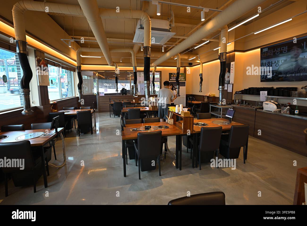 Interno moderno di un ristorante di barbecue coreano in Corea con tavoli di legno, tubi di ventilazione e disposizioni dei posti a sedere. Foto Stock