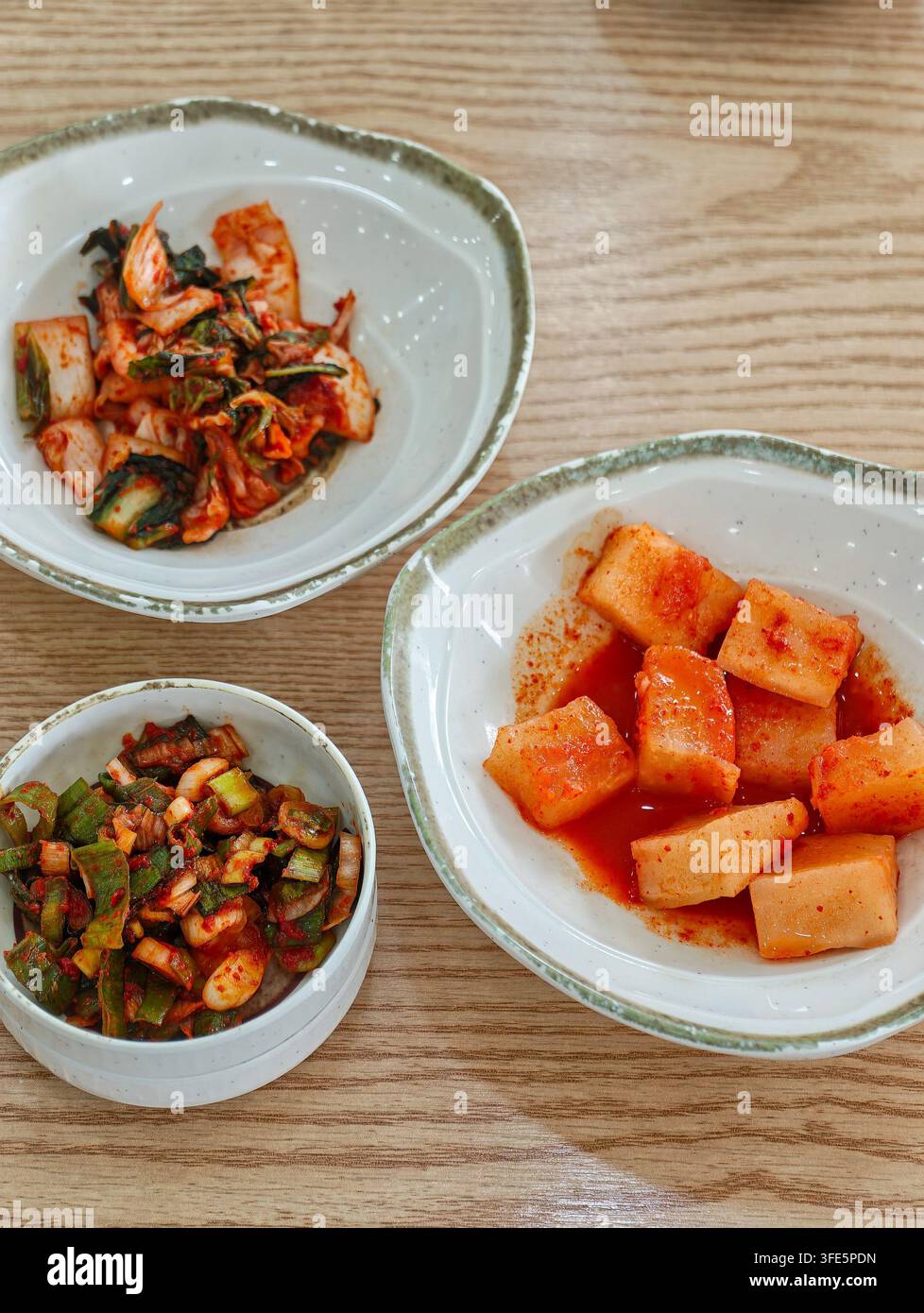 Tre ciotole di varietà tradizionali di kimchi coreano servite su un tavolo di legno, che mostrano colori e texture vivaci. Foto Stock