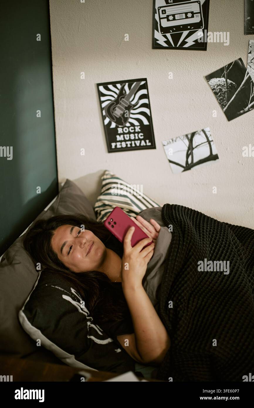 Donna biracial che si rilassa a letto e naviga sullo smartphone Foto Stock