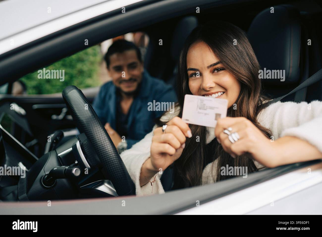 Ritratto di una giovane donna sorridente che mostra la sua patente di guida seduta in auto Foto Stock
