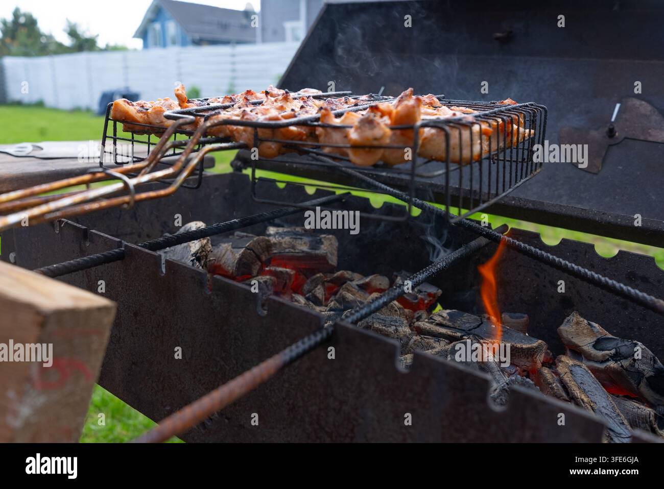 Polli grigliati che sfrigolano su un barbecue nel cortile in una vista ravvicinata allettante. Appetitosi pollami grigliati con un fascino saporito, la loro pelle dorata che luccica nella calda luce del sole sopra una recinzione suburbana. Foto Stock