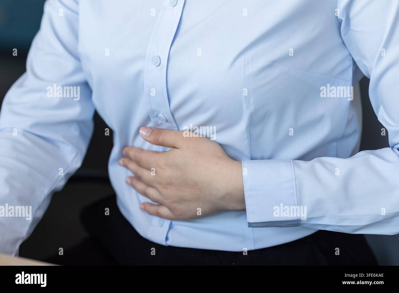 Donna d'affari che avverte un forte dolore addominale, si tiene lo stomaco mentre si sente male e a disagio per indigestione o crampi durante l'orario di lavoro in un ambiente d'ufficio Foto Stock