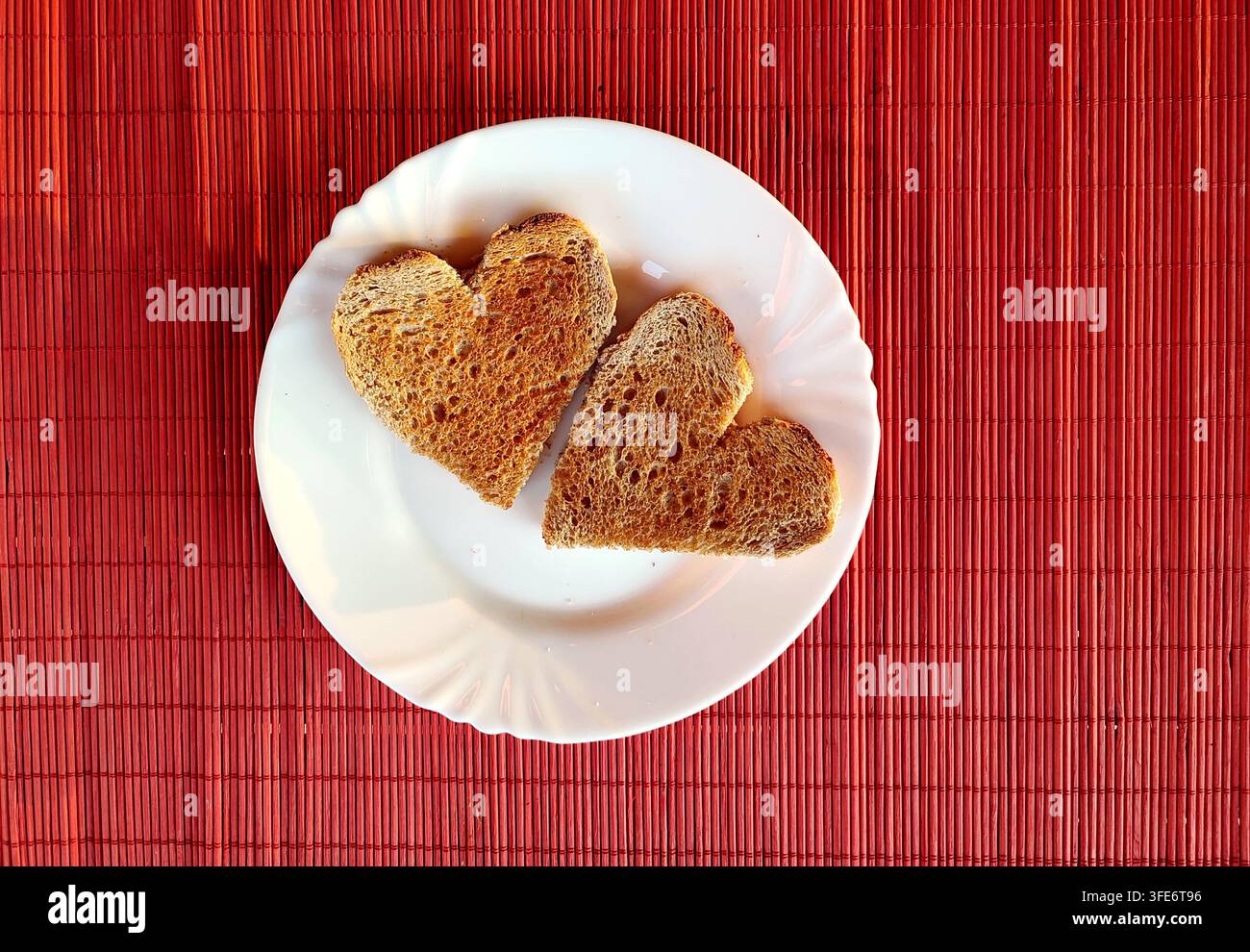 Fette di pane tostato a forma di cuore su piatto bianco. Due fette di pane tostato a forma di cuore servite su un piatto bianco su una tovaglietta di bambù rosso vivace. - Immagine stock catturata con smartphone