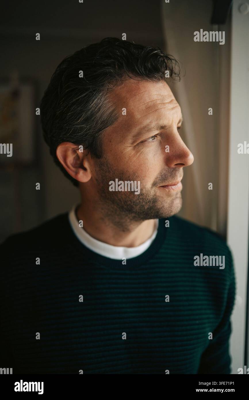 Un uomo premuroso che guarda fuori dalla finestra di casa Foto Stock