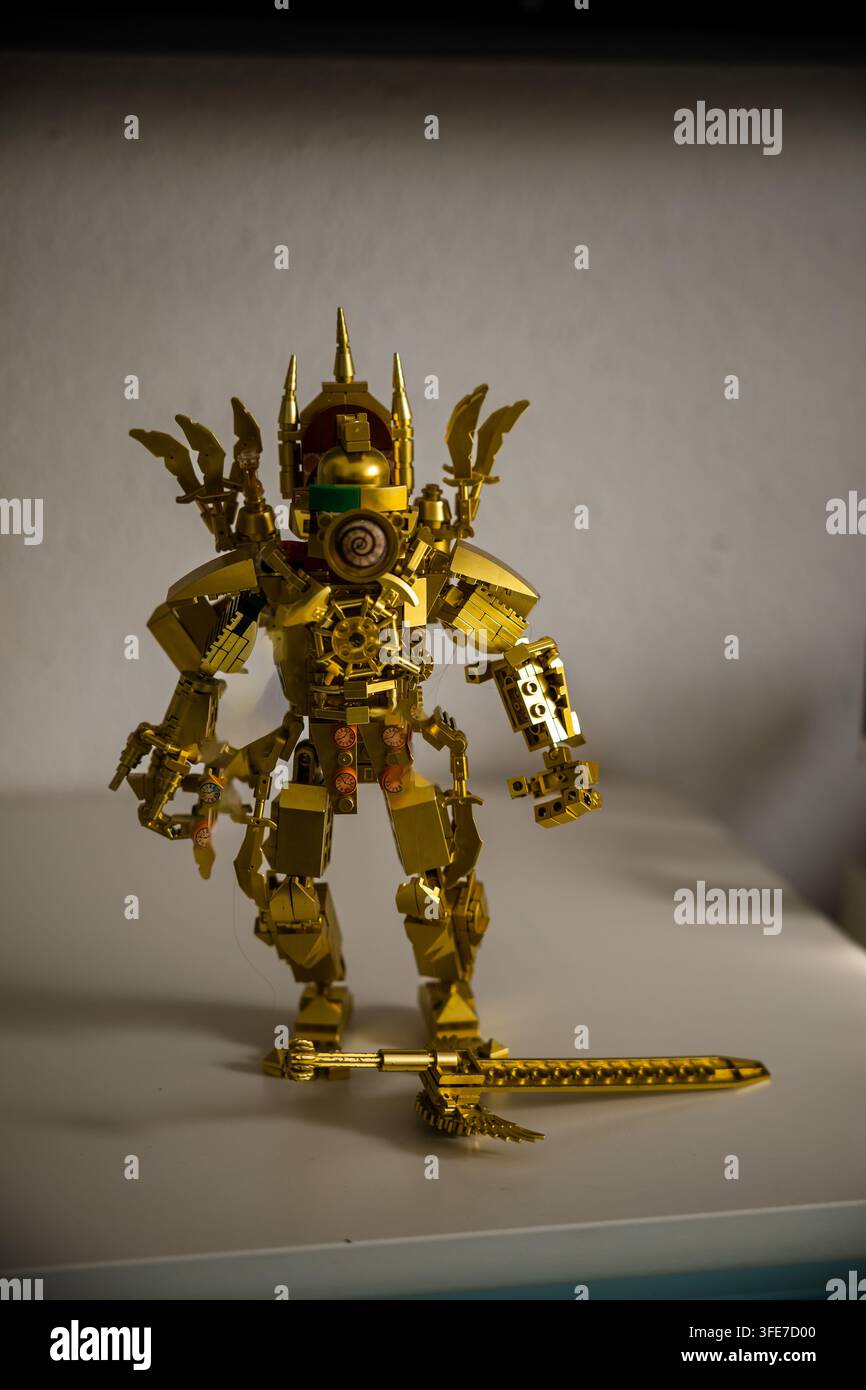 Figura Lego Golden Mech in piedi alta con una grande spada dorata a terra, costruita da un set di mattoncini di plastica metallici su un tavolo bianco. Foto Stock