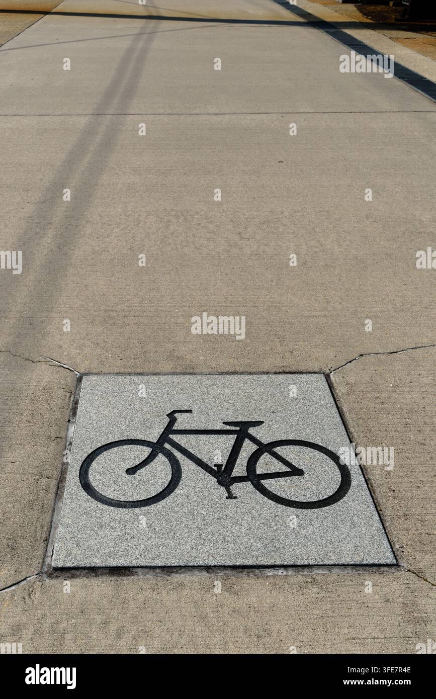 Simbolo di bicicletta inciso nella pietra su una strada asfaltata che funge da pista ciclabile, indicando la corsia corretta per i ciclisti da percorrere accanto ai pedoni Foto Stock