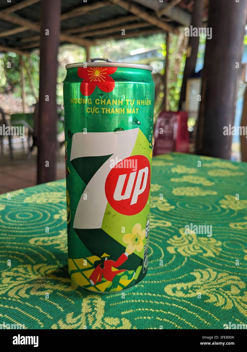 Una lattina di 7UP raffreddata con condensa si trova su una tovaglia a motivi verdi, suggerendo una bevanda fresca in una giornata calda Foto Stock