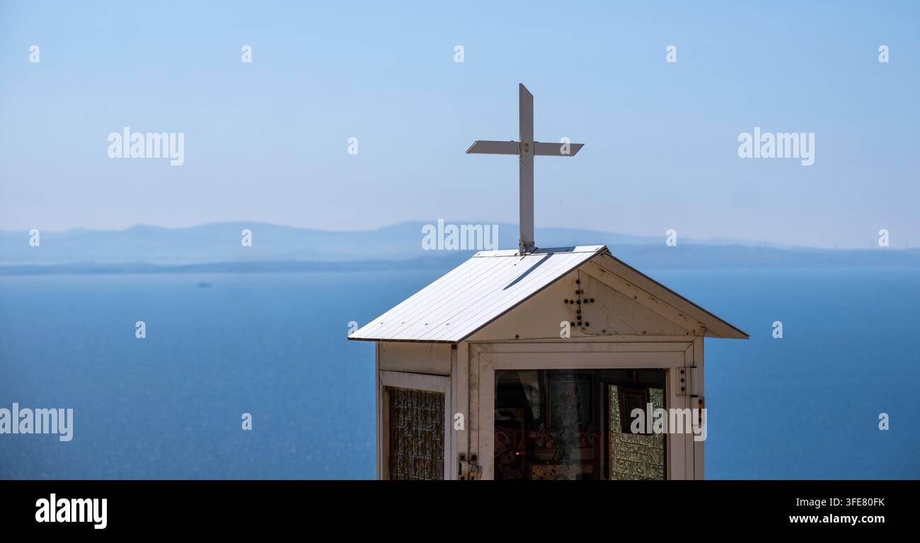 Un piccolo santuario ortodosso stradale con croce e icone di vetro si affaccia sul Mar Egeo sull'isola di Chio, Grecia, sotto un cielo azzurro Foto Stock