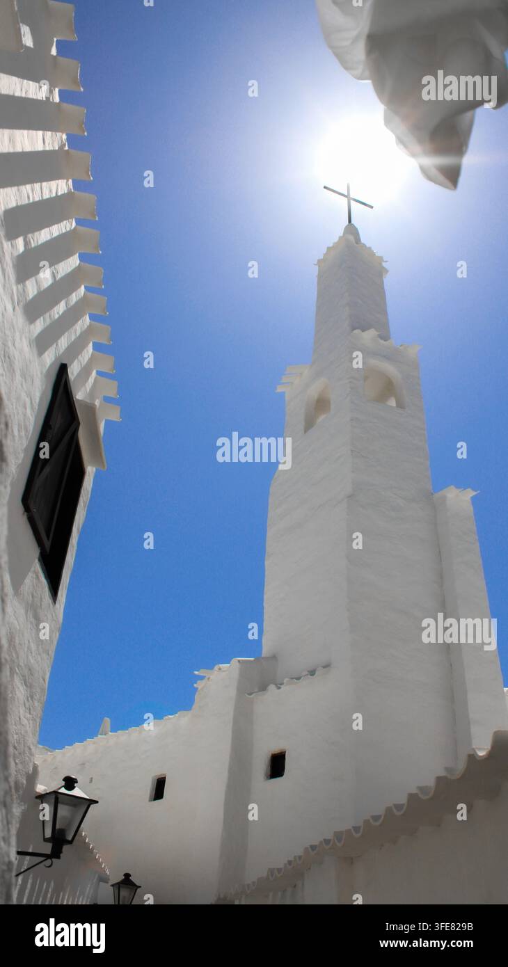 Vista del campanile bianco della chiesa nel villaggio storico sotto un cielo blu luminoso a Binibequer Vell, Illes Balears, Spagna. Foto Stock