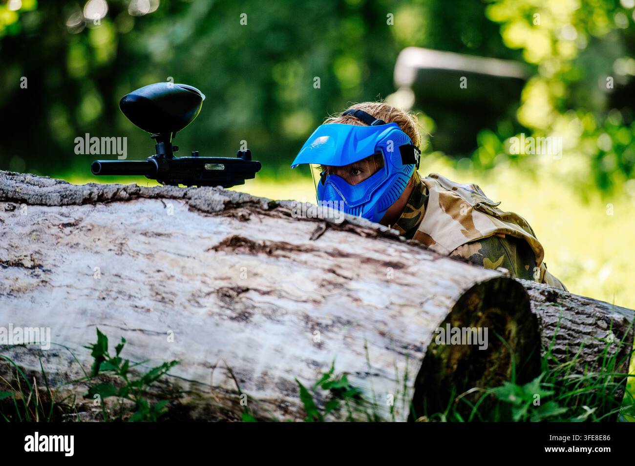 Persona che si mette al riparo dietro un tronco caduto durante una partita di paintball in un campo all'aperto Foto Stock
