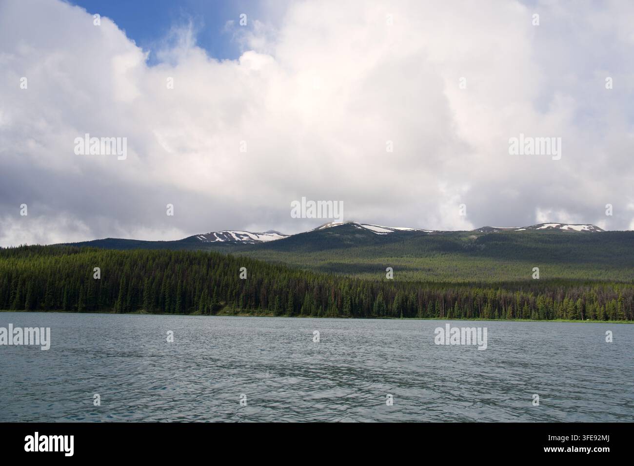 Lago montano scenografico circondato da dense foreste di pini sempreverdi sotto un drammatico cielo nuvoloso con picchi innevati a chiazze Foto Stock