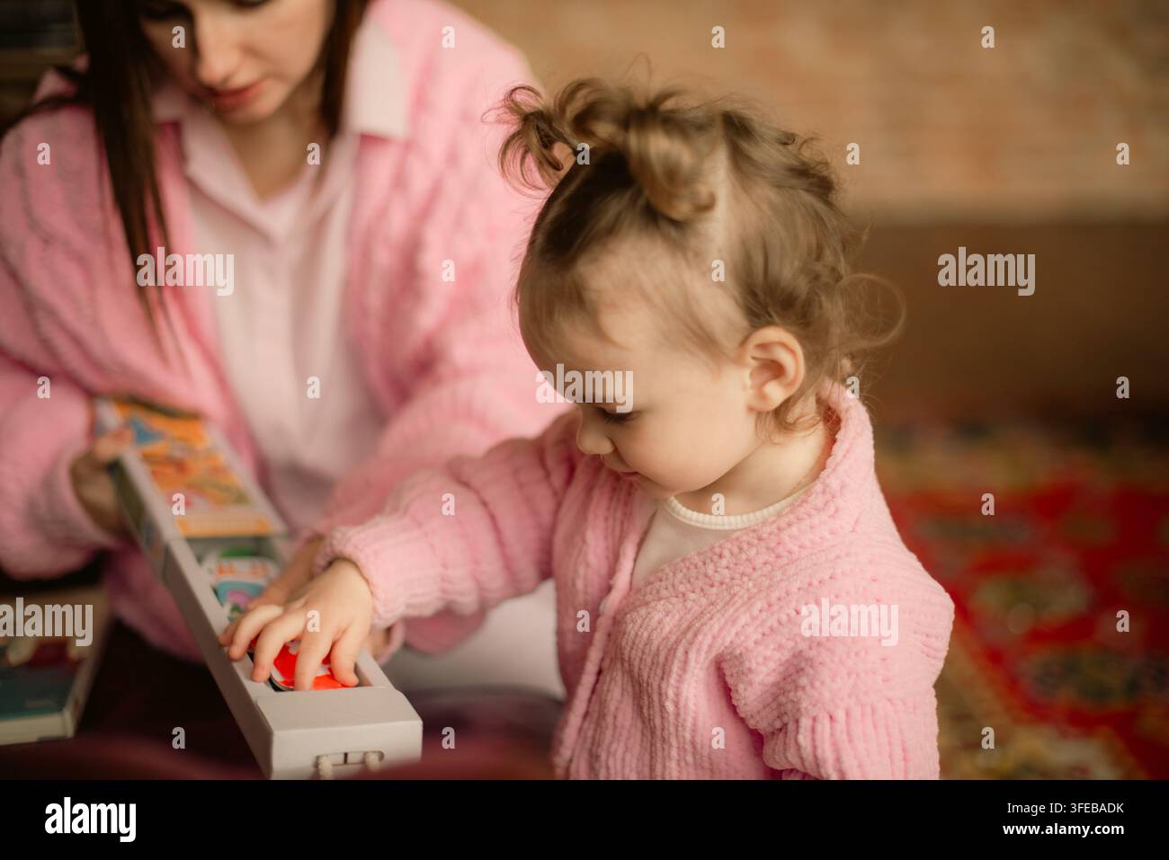 Dolce bambina che gioca con un gioco di puzzle educativo sotto la supervisione della madre a casa Foto Stock