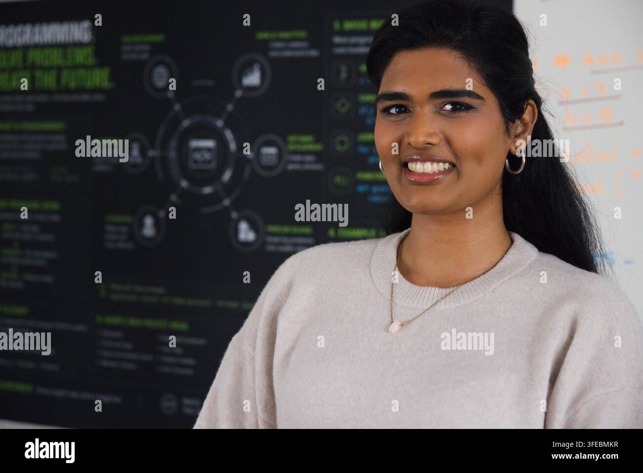Donna indiana in piedi accanto a un poster di ricerca al campus, che mostra un diagramma circolare e appunti alla lavagna Foto Stock
