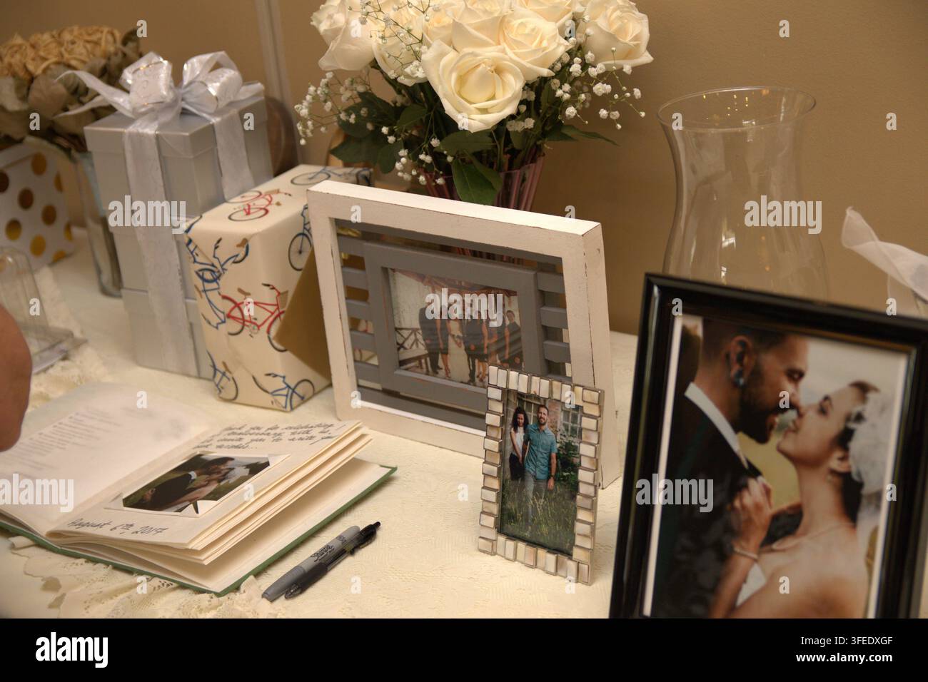 Un tavolo decorato per il libro degli ospiti del matrimonio con foto incorniciate della coppia, un mazzo di rose bianche, regali incartati e un libro degli ospiti aperto con penna Foto Stock