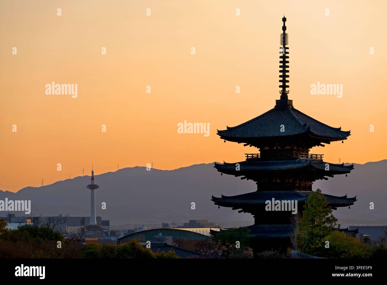 Vista al tramonto del tempio buddista giapponese Hokanji con la pagoda Yasaka a cinque piani in primo piano e montagne con la torre di Kyoto sullo sfondo, Giappone. Foto Stock