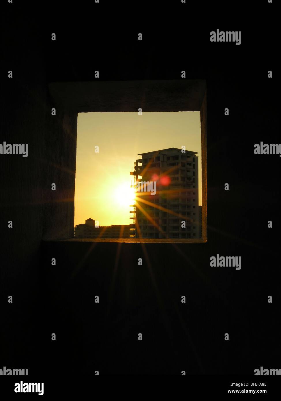 Raggi di sole al tramonto che incorniciano un cantiere di costruzione di grattacieli in ombra scura, cornice ritagliata Foto Stock